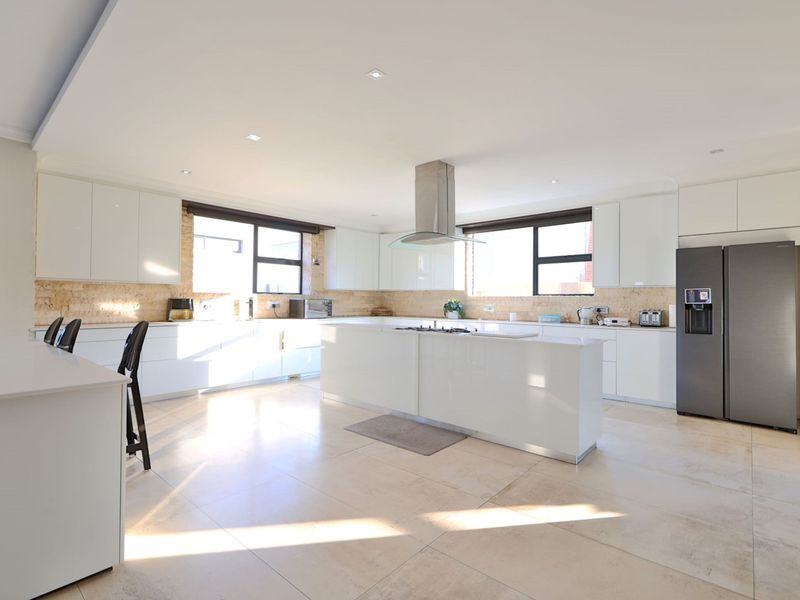 Modern, spacious kitchen featuring a large central island with a gas cooktop, sleek white cabinetry, stone countertops, and high-quality tiled flooring.