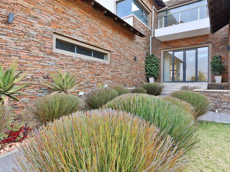 Modern architectural facade featuring extensive stacked stone cladding, a glass balcony, and a landscaped garden entrance with paved pathways.