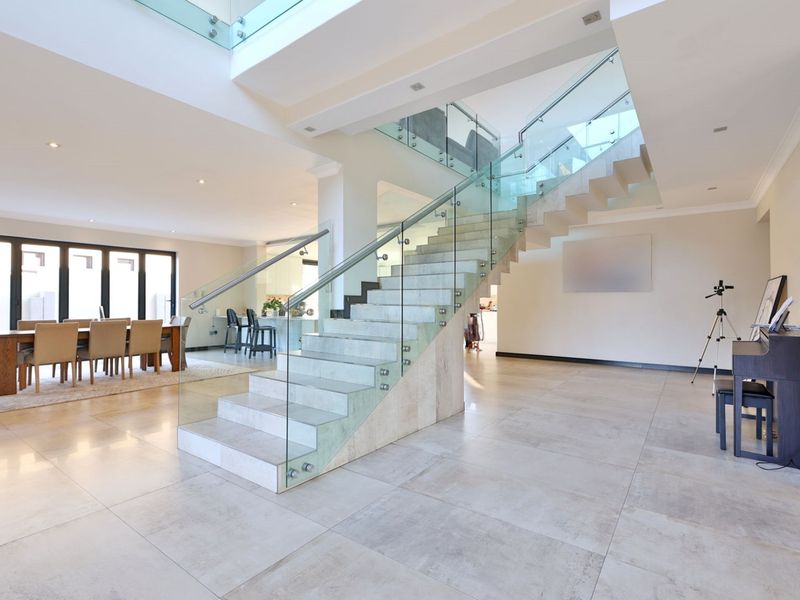 Spacious open-plan living area featuring a modern floating staircase with glass balustrades, large format floor tiles, and seamless access to the outdoor patio.