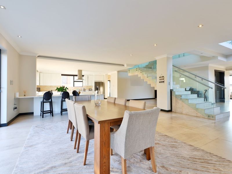 Spacious open-plan living and dining area featuring a modern kitchen, sleek tiled floors, and a contemporary staircase with glass balustrades.