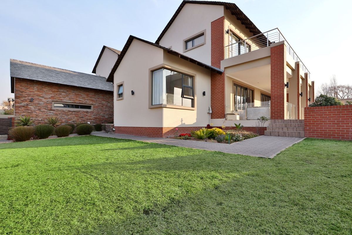Rear view of a modern double-story house featuring a brick facade, a spacious balcony, and a well-maintained garden with a paved walkway.
