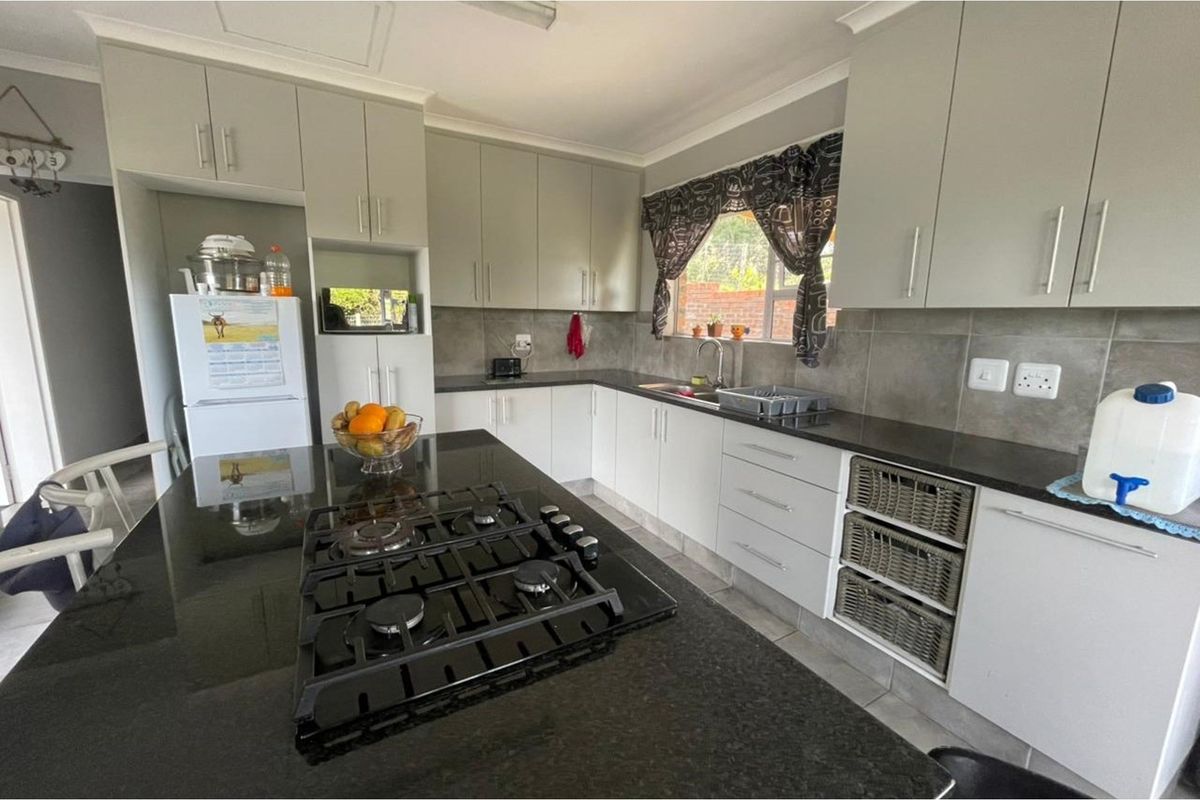Modern kitchen featuring light grey cabinetry, dark granite countertops, a central island with a gas hob, and tiled backsplash.