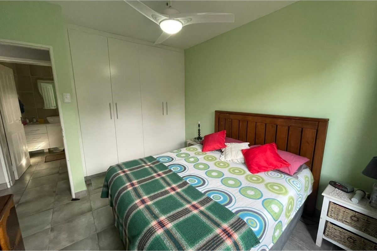 A bedroom featuring built-in cupboards, a ceiling fan, and tiled flooring, with an adjoining bathroom visible through the doorway.