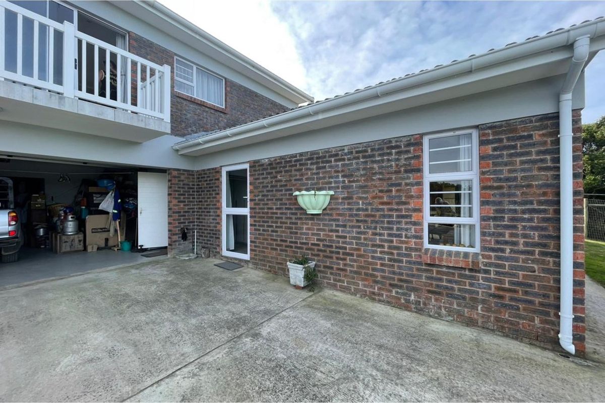 Rear exterior view of the property featuring a brick facade, concrete patio area, and an upper-level balcony with white railings.