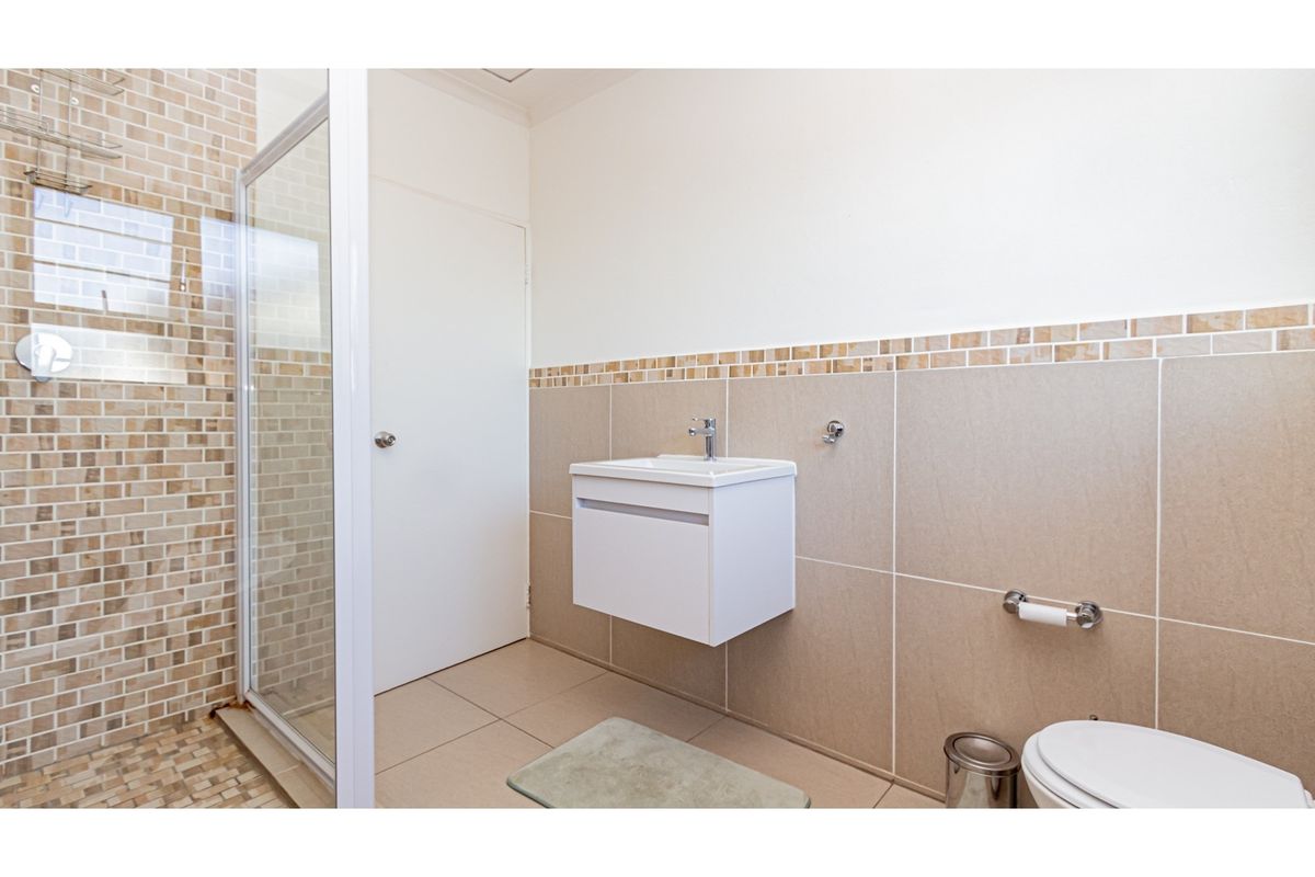 A modern bathroom featuring a glass-enclosed shower, wall-mounted vanity with basin, and neutral tiled walls with decorative mosaic accents.