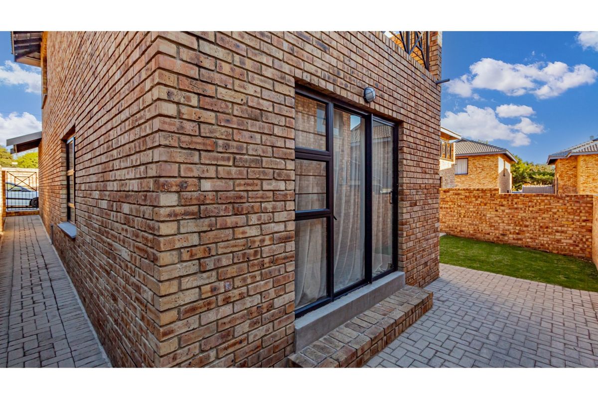 A view of the rear exterior of the townhouse, featuring face-brick walls, paved patio area, and a small garden space.