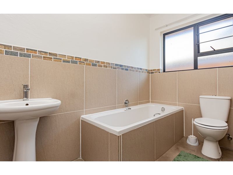 A clean and functional bathroom featuring a pedestal basin, built-in bathtub, and toilet, finished with neutral wall tiles and a decorative mosaic border.