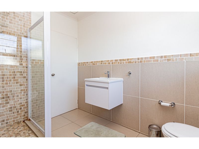 A clean, modern bathroom featuring a glass-enclosed shower, wall-mounted vanity with basin, and neutral tiled finishes throughout.