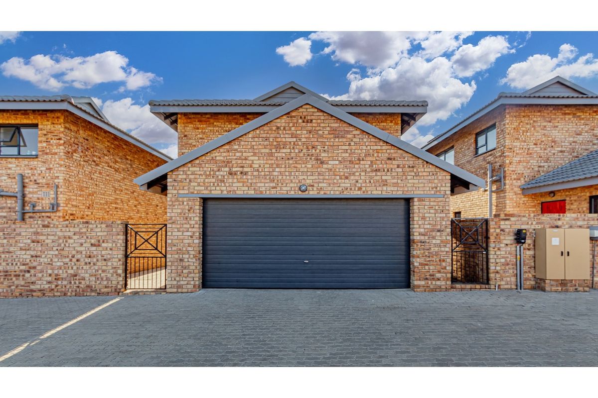 A well-maintained townhouse exterior featuring a face brick facade, a secure automated garage door, and a paved driveway with side pedestrian access.