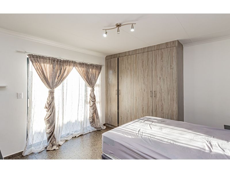 A bright bedroom featuring built-in wood-finish wardrobes, tiled flooring, and a sliding glass door providing natural light.