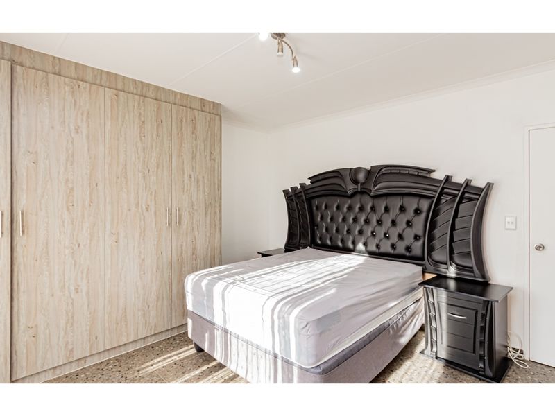 A well-maintained bedroom featuring light wood-grain built-in cupboards, terrazzo flooring, and a modern spotlight fixture.