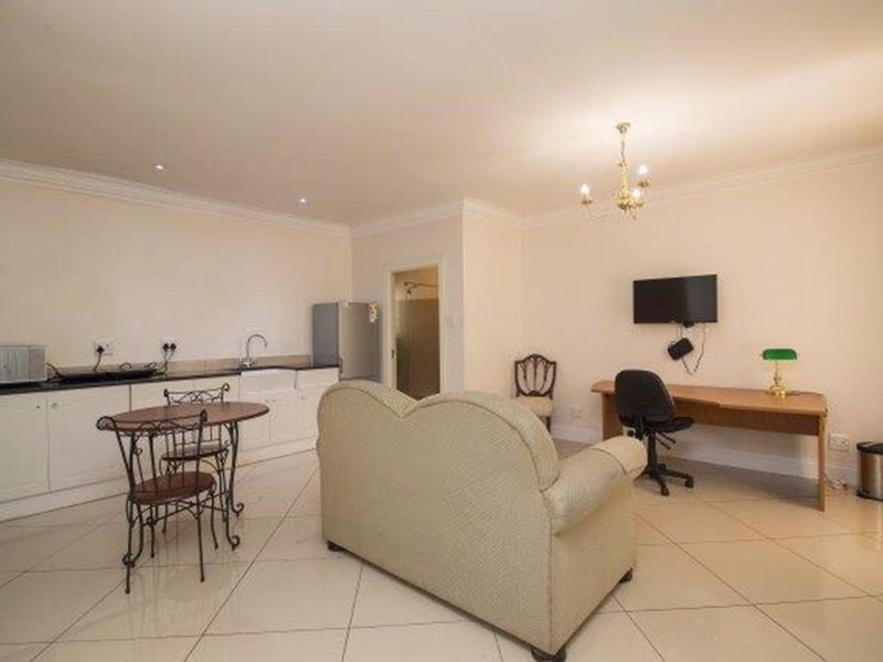 Open-plan living area featuring a kitchenette with cabinetry, apron sink, and tiled flooring, suitable for a studio or multi-functional living space.