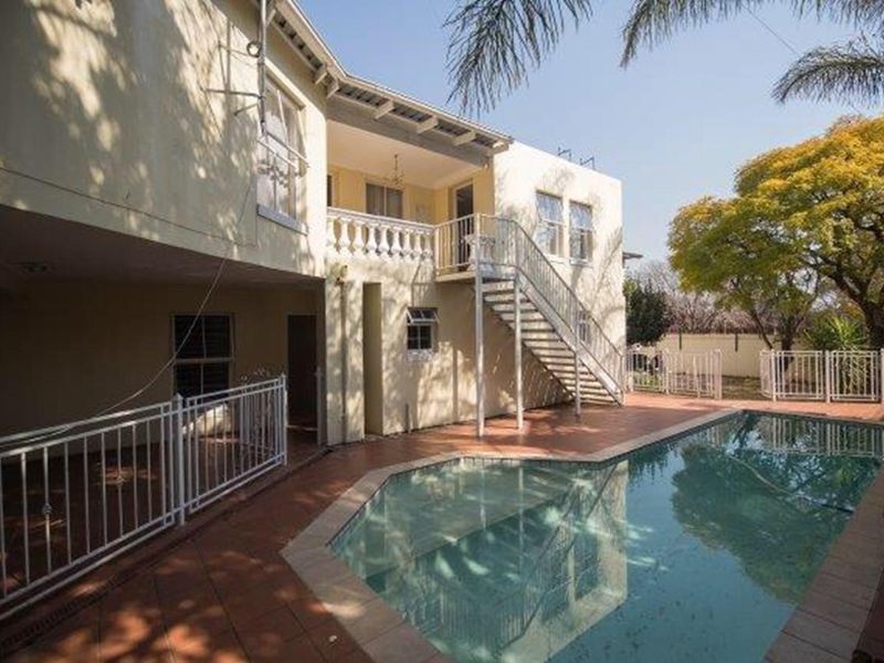 Rear exterior view featuring a swimming pool, tiled patio area, and an external staircase leading to an upper-level balcony.