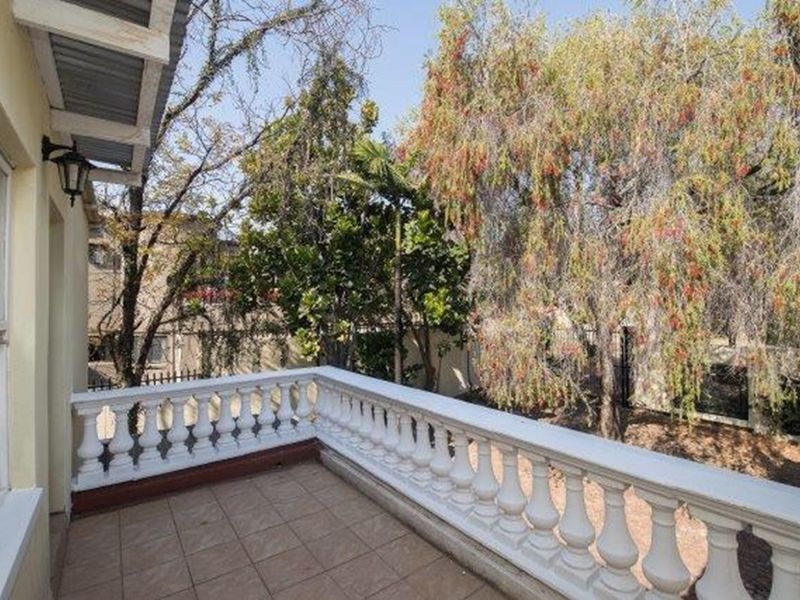 An elevated balcony featuring a classic balustrade and tiled flooring, overlooking a mature garden area.