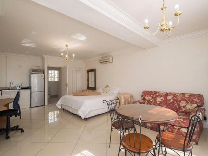 An open-plan studio apartment featuring tiled flooring, crown molding, a compact kitchenette, and a split-system air conditioner.