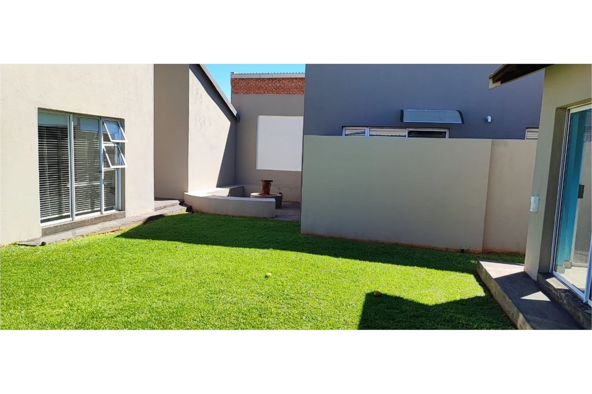 A private rear courtyard featuring a well-maintained lawn, paved seating area with a built-in feature, and modern exterior wall finishes.