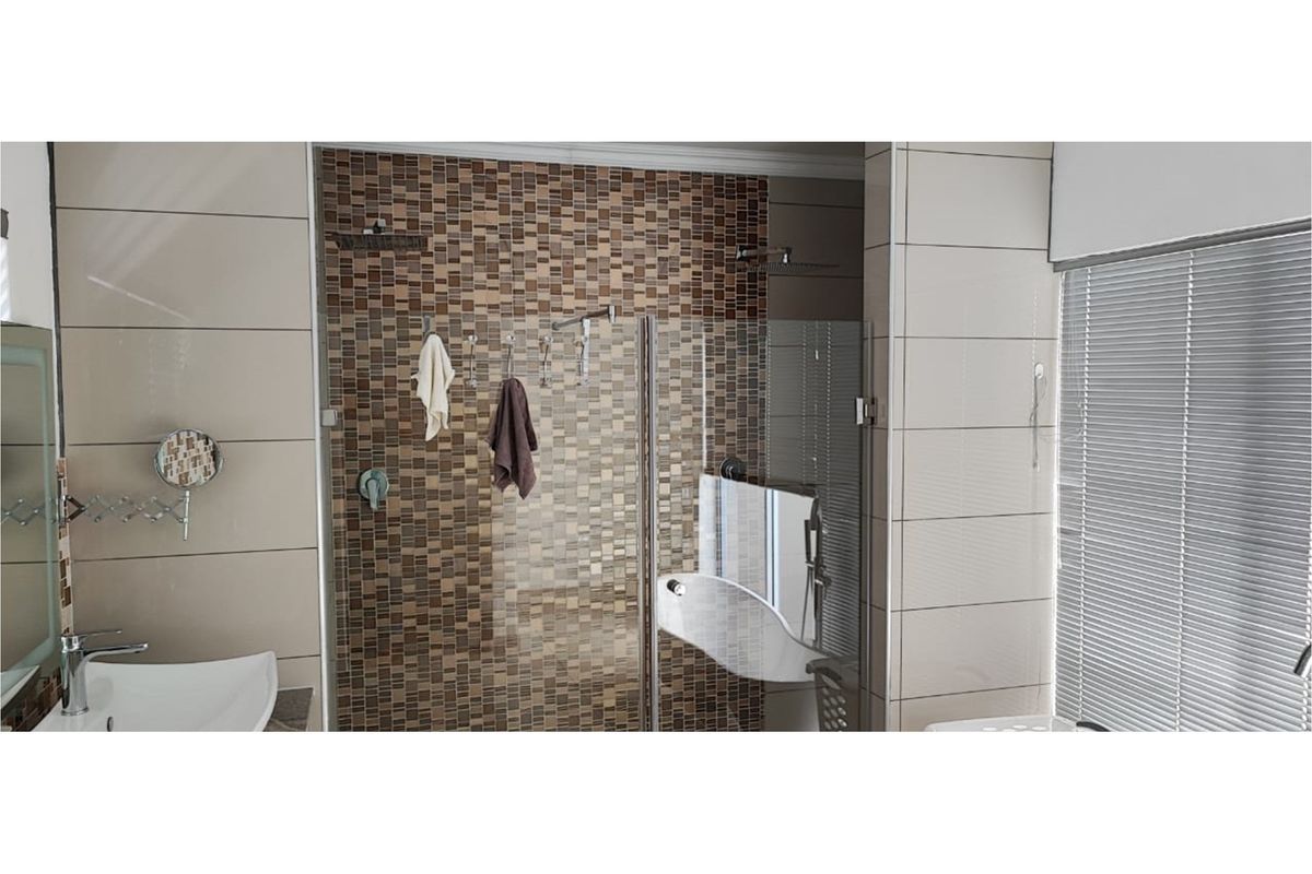 Modern bathroom featuring a glass-enclosed shower with mosaic tile accent wall, contemporary basin, and fitted window blinds.