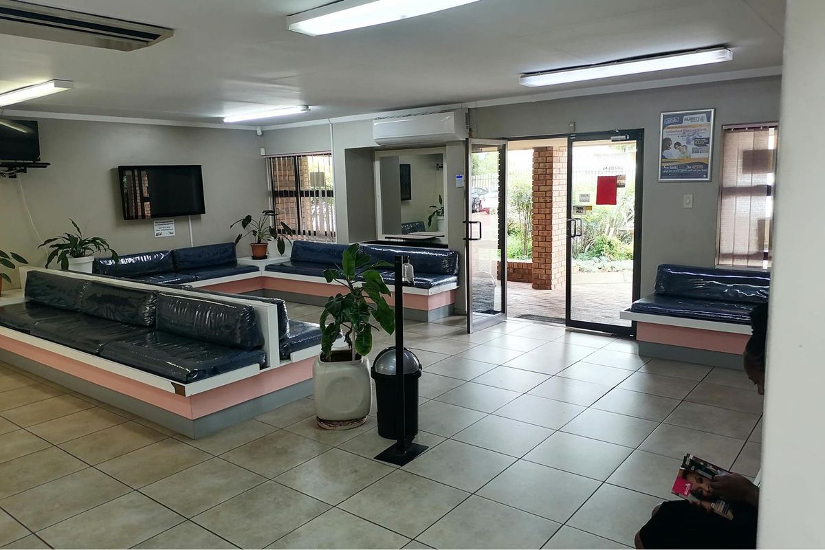 A spacious waiting area featuring tiled flooring, built-in bench seating, and a glass-panelled entrance door leading to an outdoor patio.
