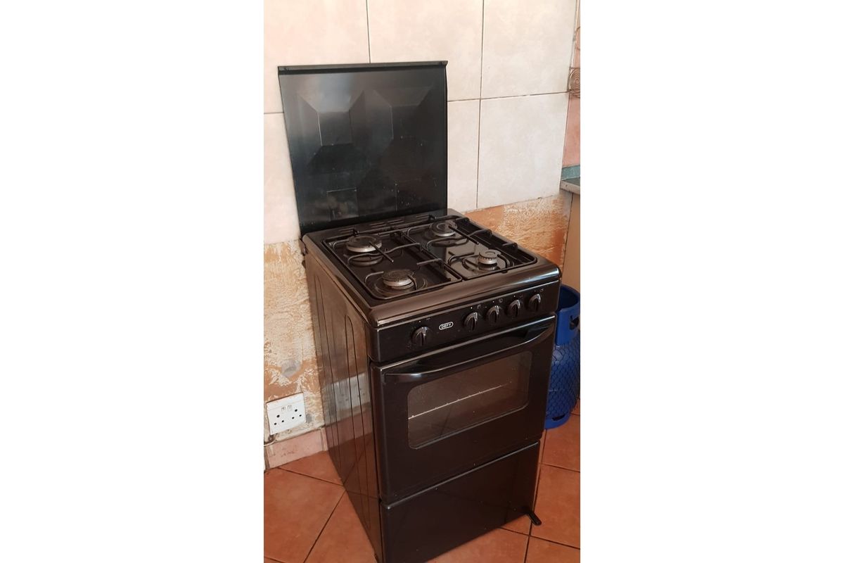 A freestanding black gas stove positioned against a tiled wall in a kitchen area.
