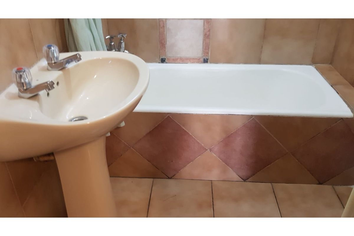 A dated bathroom featuring a pedestal basin and a tiled bathtub surround with neutral-toned ceramic wall and floor tiles.
