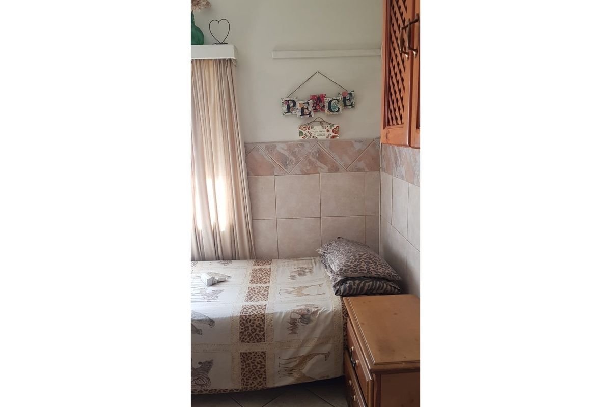 A compact bedroom featuring tiled wall accents, built-in wooden cabinetry, and a window with curtains.