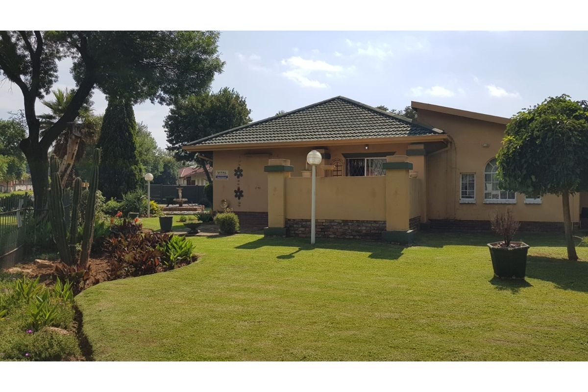 A view of the rear garden and patio area featuring a well-maintained lawn, established landscaping, and a covered outdoor space.