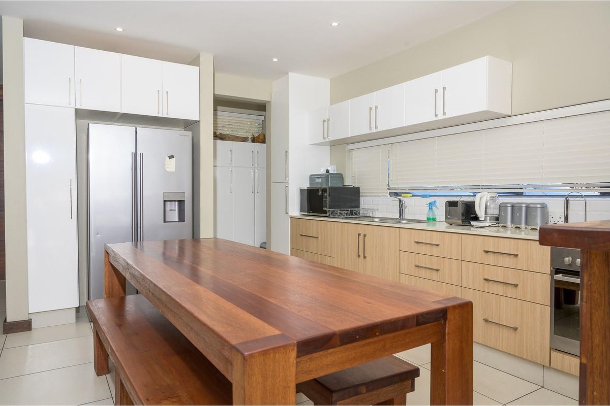 Modern kitchen featuring light wood cabinetry, white upper cabinets, tiled flooring, and a built-in oven with integrated hob.