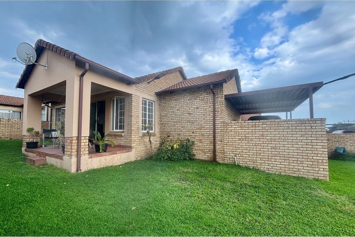 Rear view of the townhouse featuring a covered patio, face-brick exterior, tiled roof, and a private garden area.