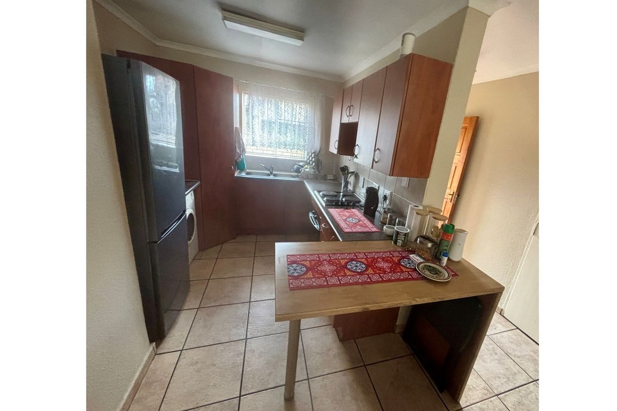 A functional kitchen featuring wooden cabinetry, tiled flooring, a built-in hob, and a double sink with a window view.