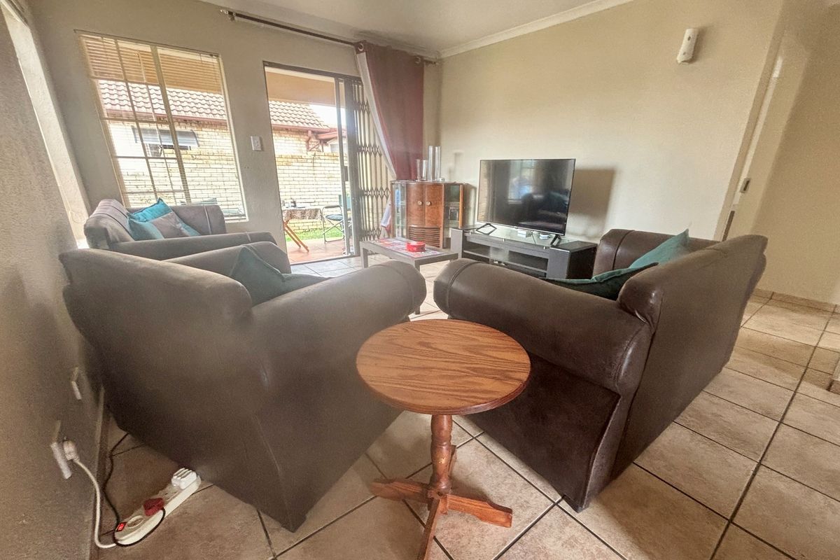 A living room featuring tiled flooring, large windows, and a sliding door providing access to an outdoor patio area.