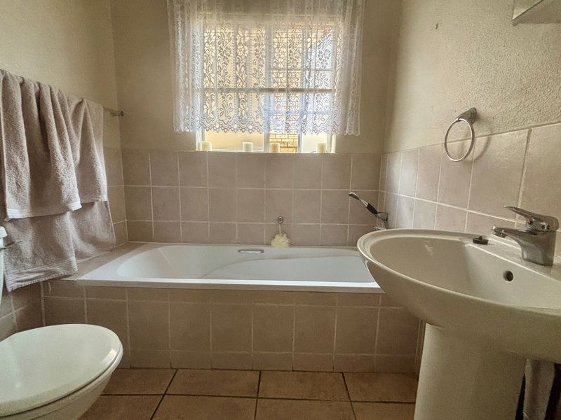 A functional bathroom featuring a built-in bathtub with tiled surround, a pedestal basin, and a standard toilet.