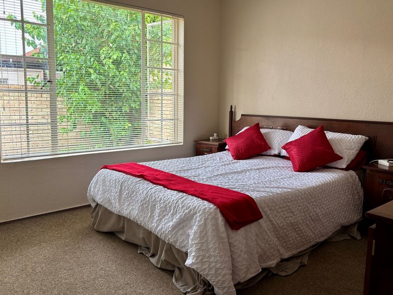 A standard bedroom featuring neutral wall tones, carpeted flooring, and a large window with fitted blinds providing natural light.