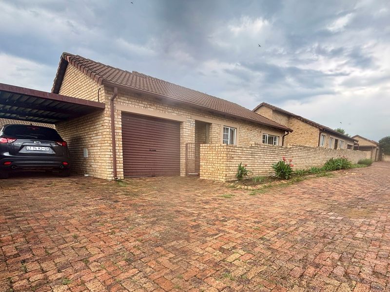 Front exterior view of a brick townhouse featuring a paved driveway, a covered carport, and a single garage with a roll-up door.