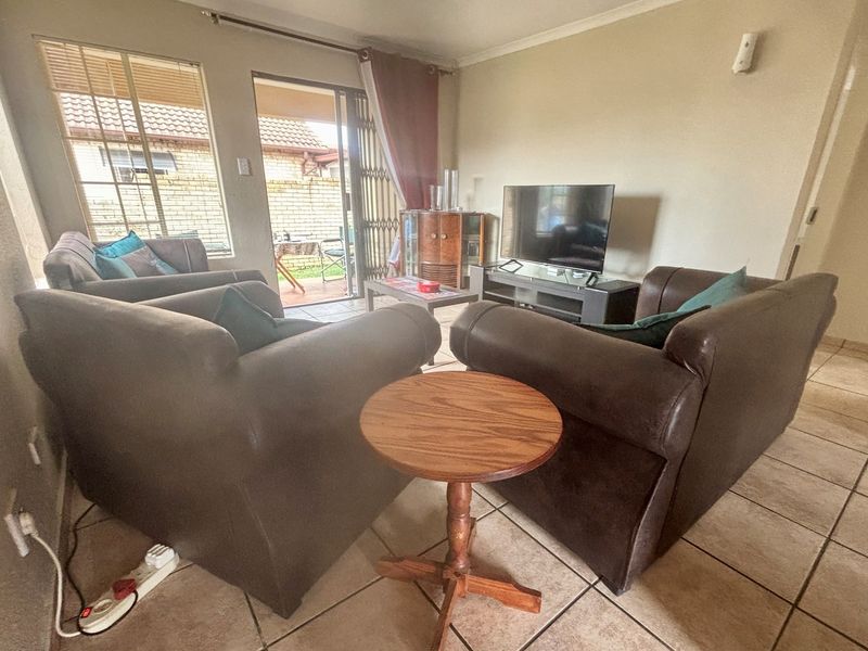 A living room featuring tiled flooring, large windows, and a sliding door providing access to an outdoor patio area.