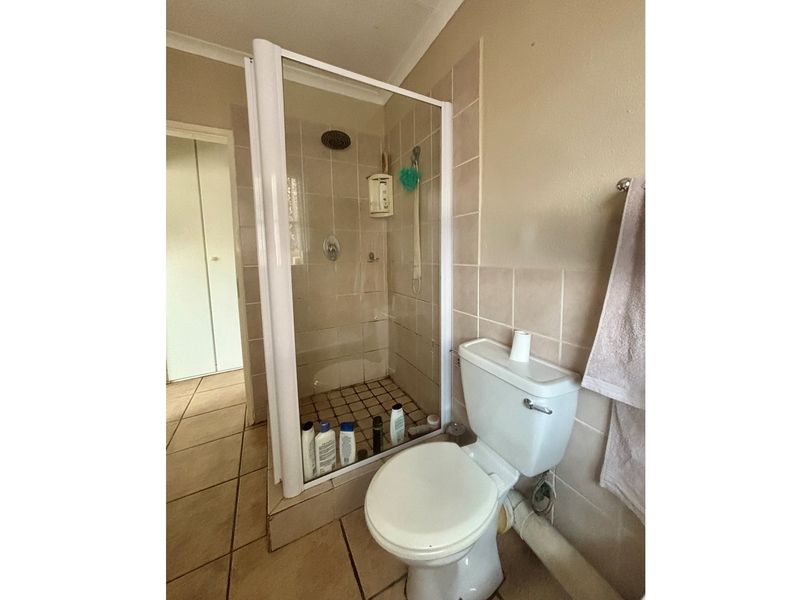 A functional bathroom featuring a corner shower enclosure with glass door, ceramic floor tiles, and a standard toilet suite.