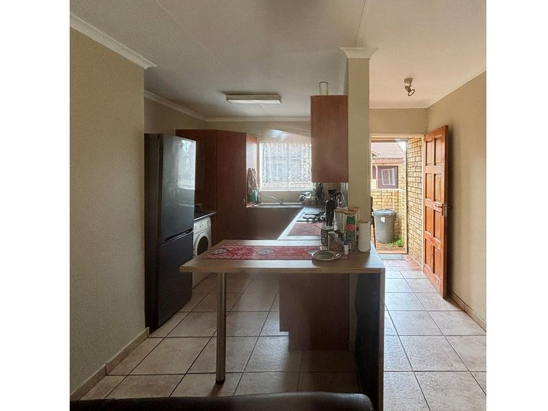 A functional kitchen featuring wooden cabinetry, a breakfast bar, and direct access to an outdoor area with tiled flooring throughout.