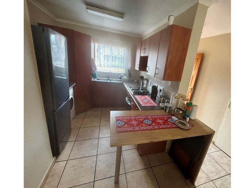 A functional kitchen featuring wooden cabinetry, tiled flooring, a built-in hob, and a double sink with a window view.