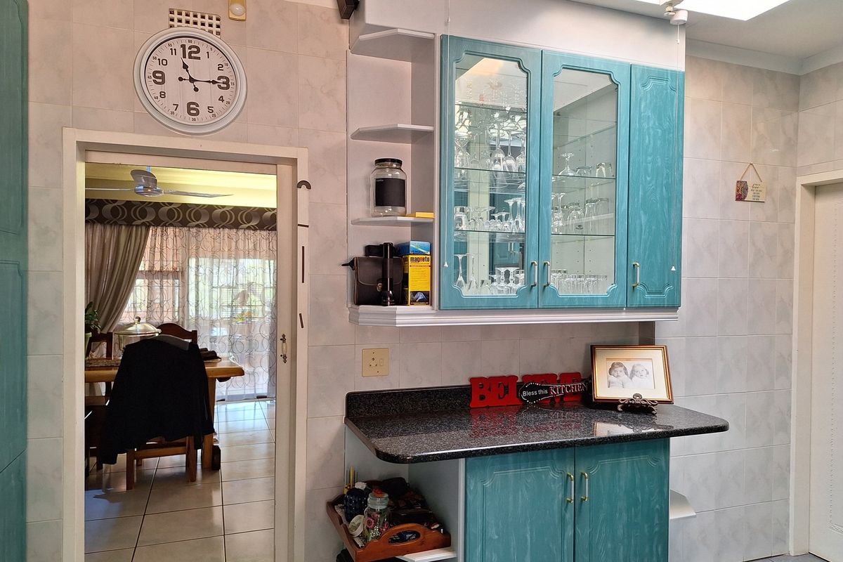 A kitchen area featuring blue cabinetry, glass-fronted display cupboards, and a dark granite-style countertop, with a doorway leading into an adjacent dining space.