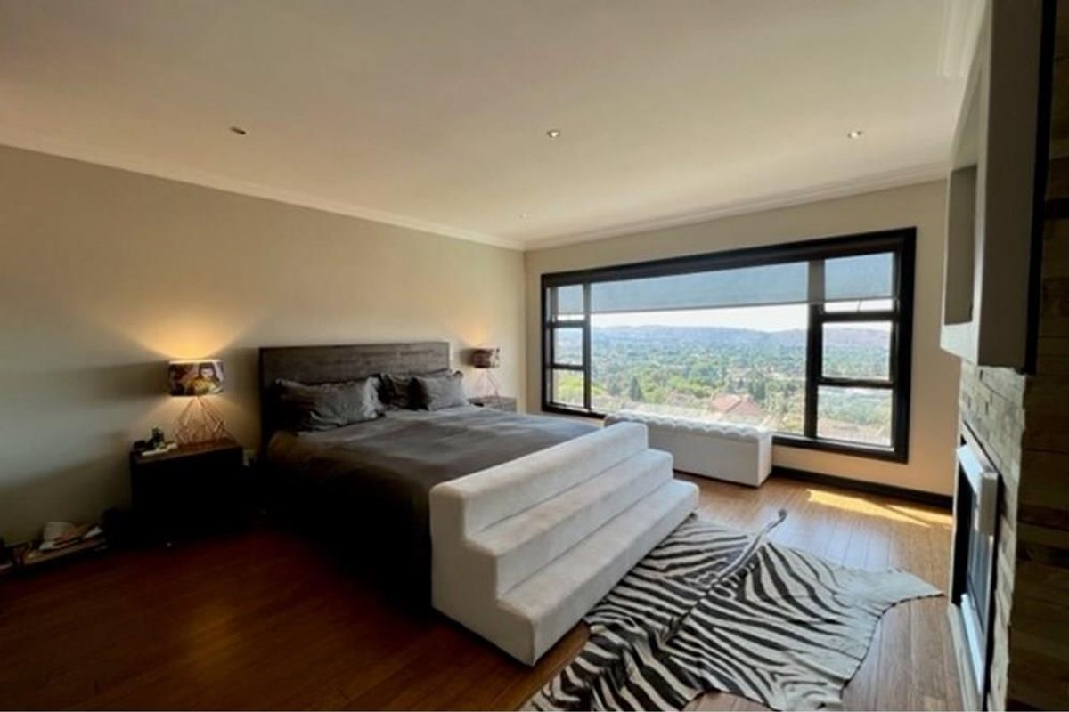 Spacious bedroom featuring hardwood flooring, recessed lighting, a built-in fireplace with stone cladding, and large windows offering expansive elevated views.