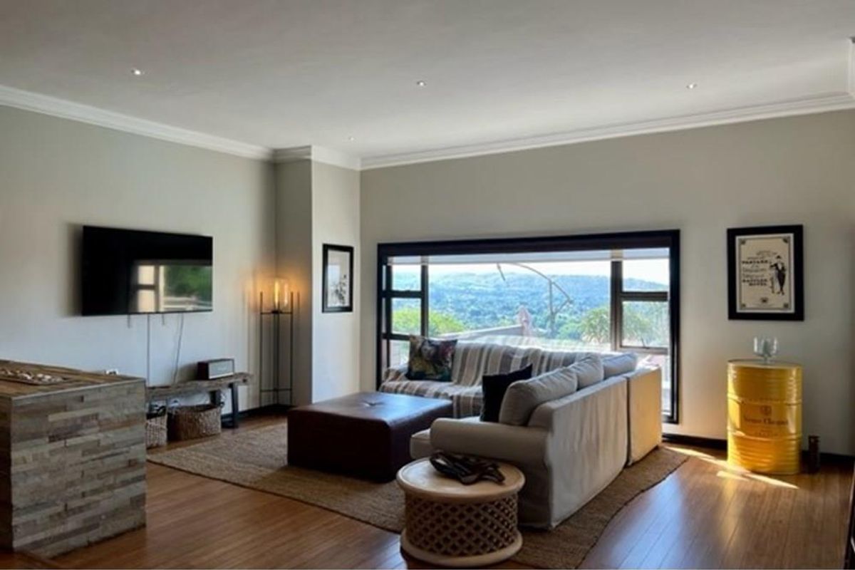 Spacious living room featuring polished timber flooring, recessed downlighting, and a large picture window offering scenic elevated views.