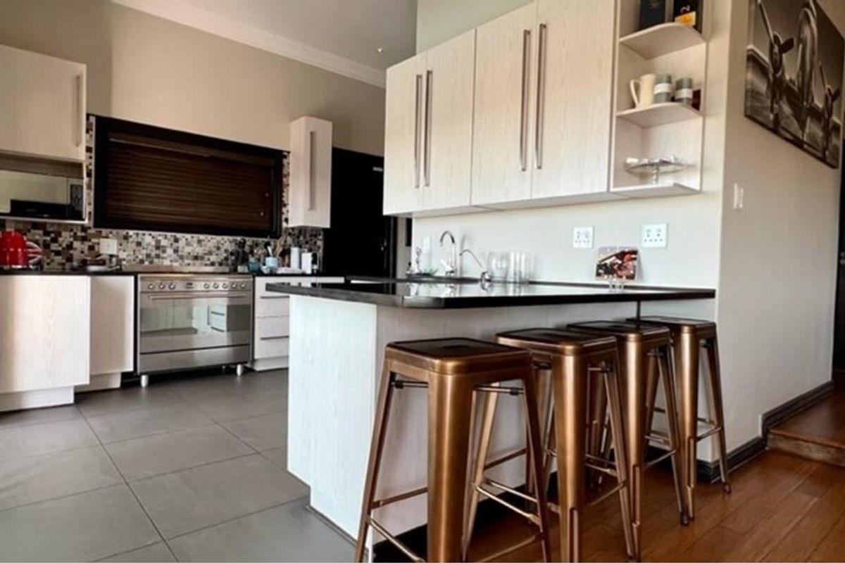 Modern kitchen featuring light wood cabinetry, dark stone countertops, a breakfast bar, and a stainless steel freestanding oven with a mosaic tile backsplash.