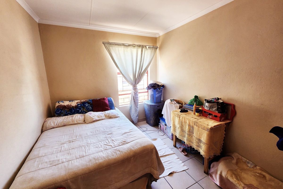 A compact bedroom featuring tiled flooring and a window fitted with security bars, offering a functional space ready for cosmetic updates.