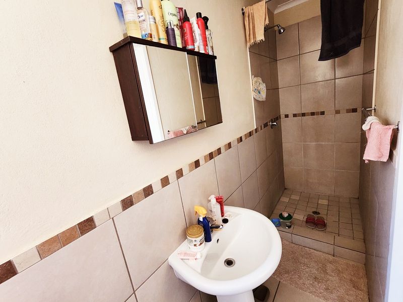 A functional bathroom featuring a pedestal basin, a tiled shower enclosure, and a wall-mounted medicine cabinet with neutral wall finishes.