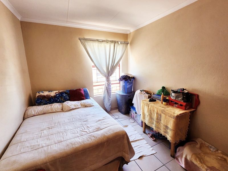 A compact bedroom featuring tiled flooring and a window fitted with security bars, offering a functional space ready for cosmetic updates.