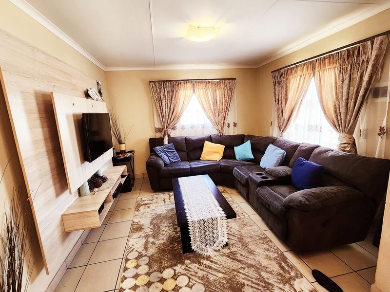 A comfortable living room featuring tiled flooring, a modern built-in media wall unit, and dual windows with curtain rails.