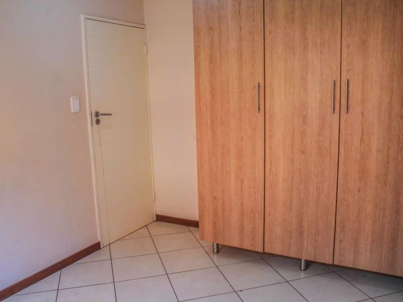 A bedroom featuring light-colored floor tiles and a large, built-in wooden wardrobe with modern metal handles.