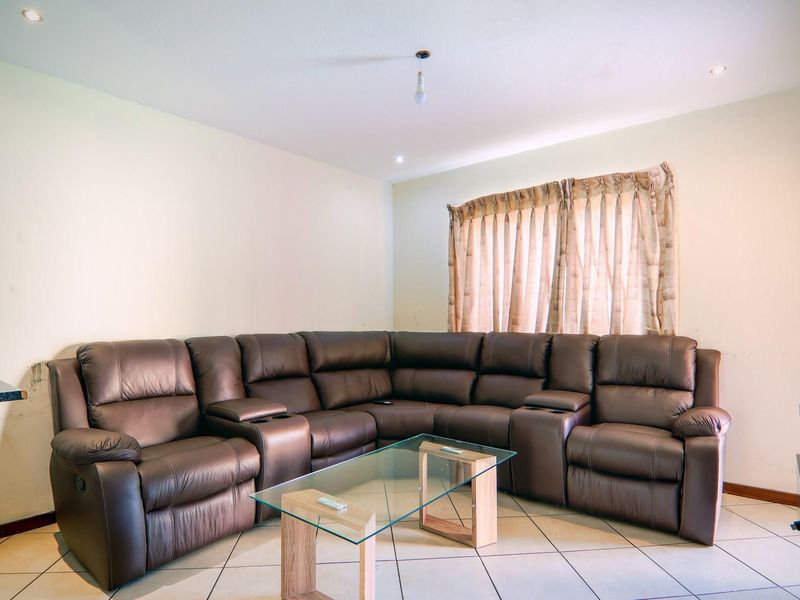 A living room featuring tiled flooring, recessed ceiling lighting, and a window with curtains.