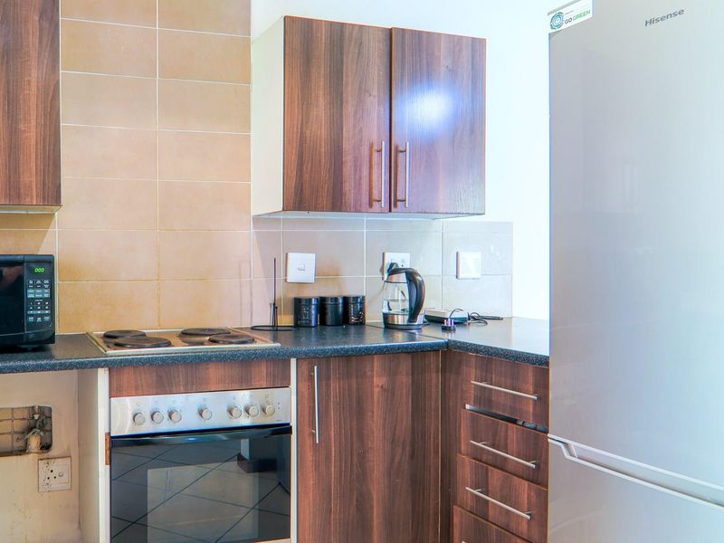 Compact kitchen featuring dark wood-look cabinetry, tiled backsplash, built-in oven, and electric hob, requiring minor repairs to cabinetry and wall finishes.