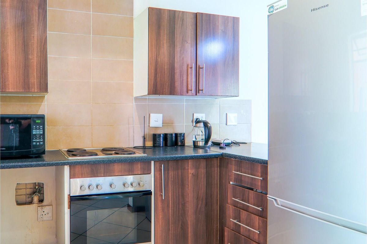 Compact kitchen featuring dark wood-look cabinetry, tiled backsplash, built-in oven, and electric hob, requiring minor repairs to cabinetry and wall finishes.