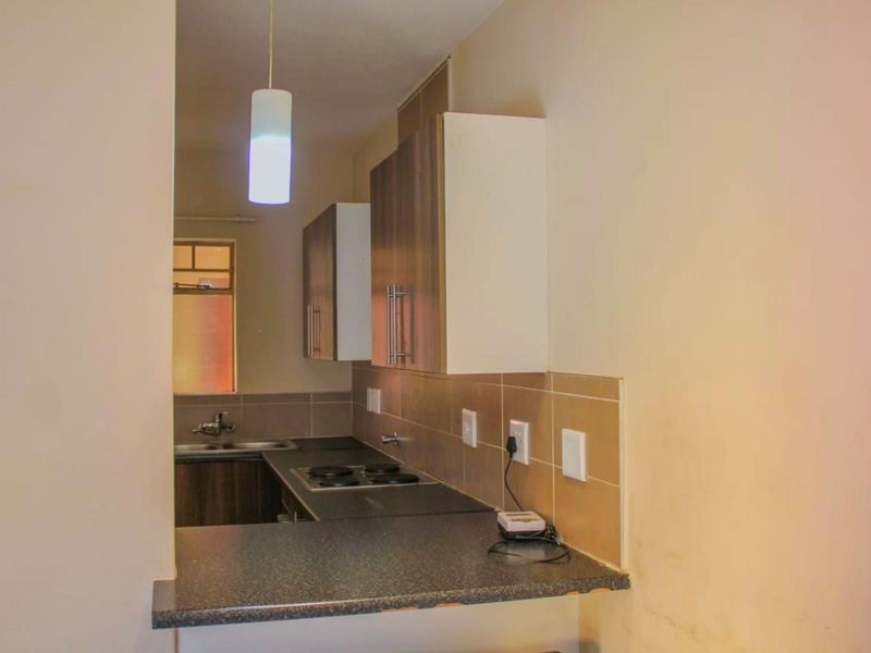 Compact kitchen featuring dark laminate countertops, built-in cabinetry, a fitted electric hob, and a stainless steel sink with tiled splashbacks.